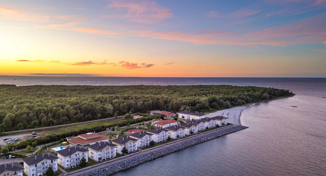Luftaufnahme eines Resorts mit weißen Gebäuden an der Küste bei Sonnenuntergang