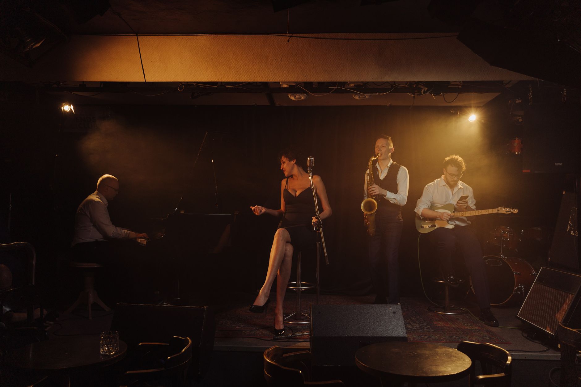 Jazz band performing on stage with pianist, female vocalist, saxophonist, and guitarist in warm amber lighting