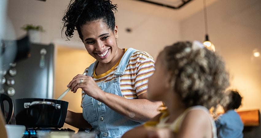 Vrouw in gestreepte shirt en spijkerjack kookt met kinderen in moderne keuken