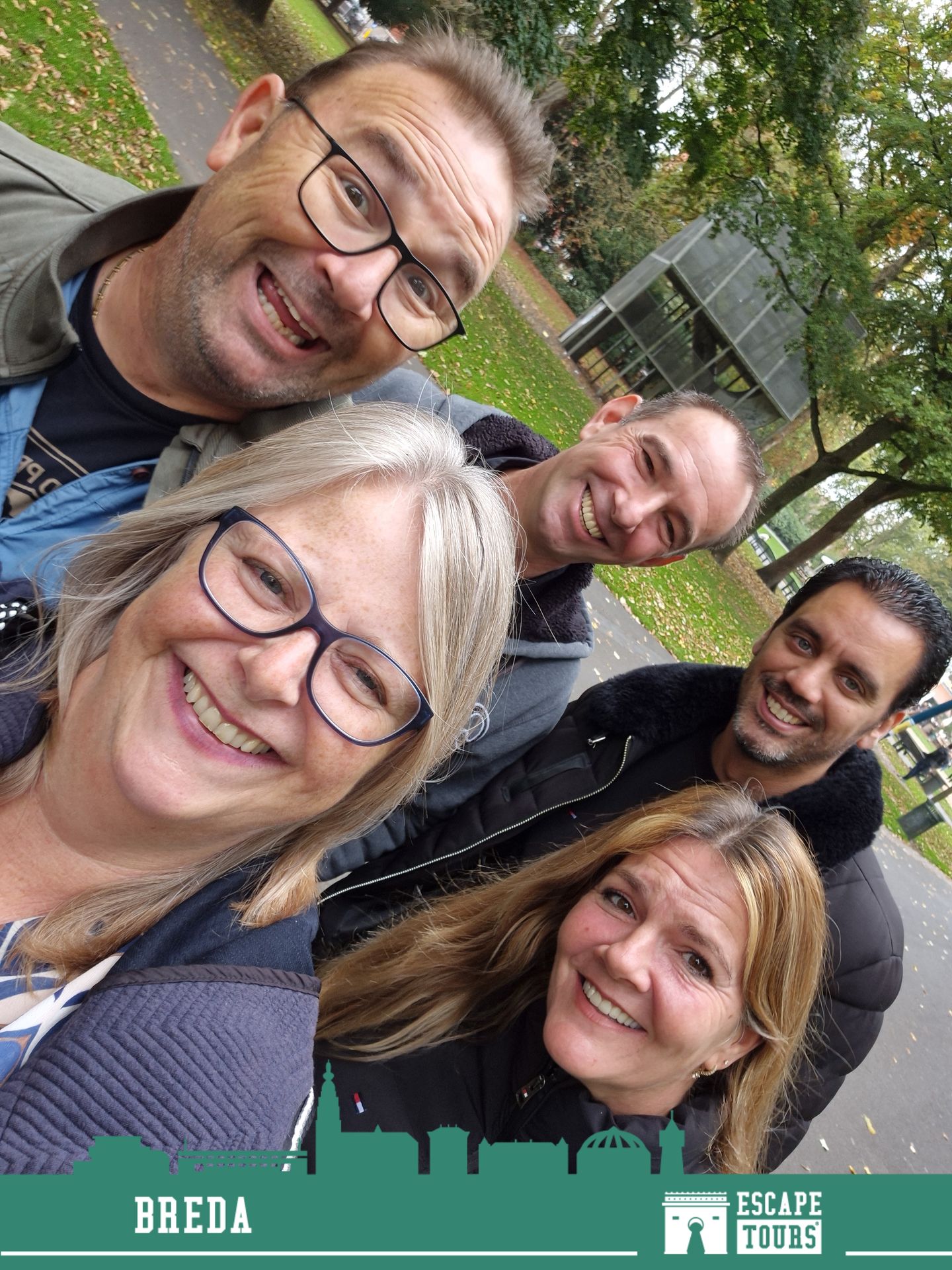 Five people smiling at the camera in a close-up selfie outdoors with green foliage visible