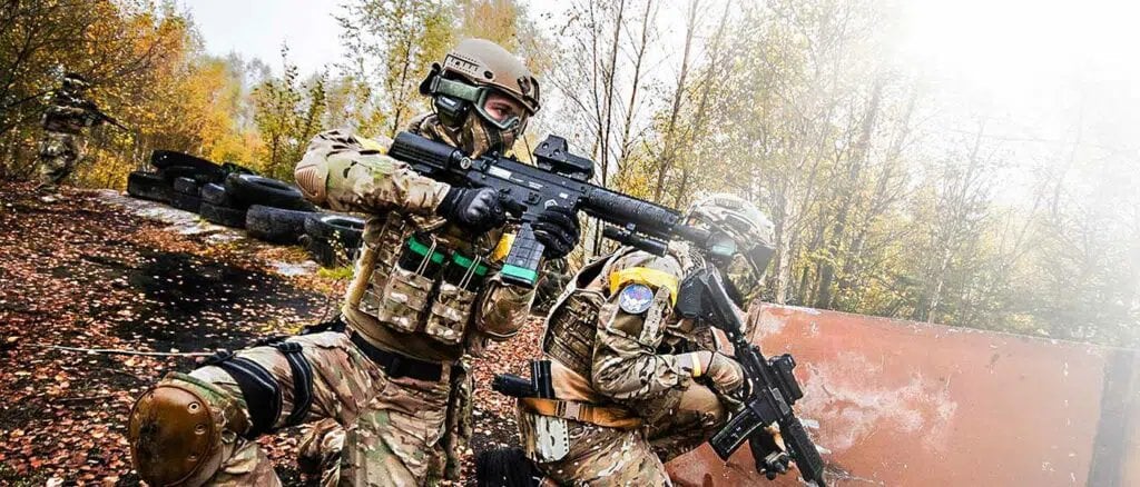 Nahaufnahme eines Paintball-Spielers in Camouflage mit Helm, der sein Markiergewehr zielt und anvisiert.