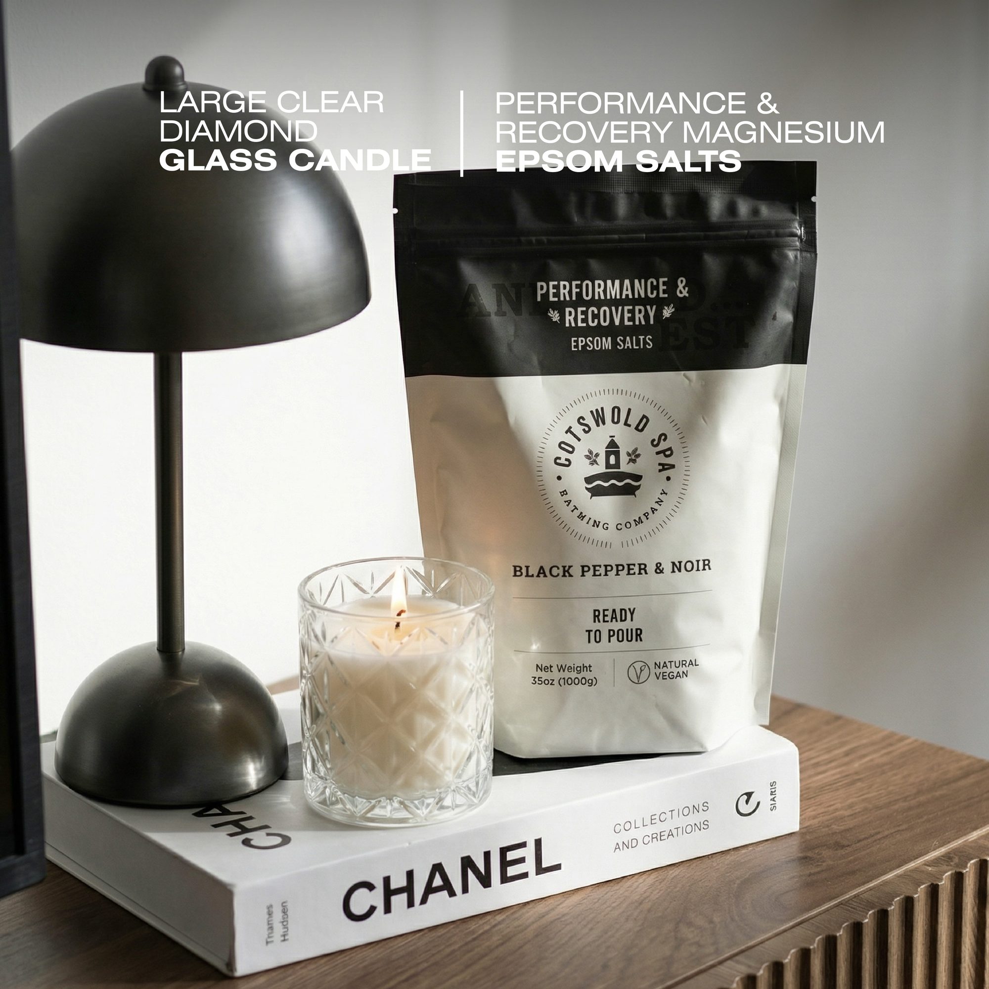 Black dome lamp next to clear diamond-cut glass candle and bag of black pepper epsom salts on white book