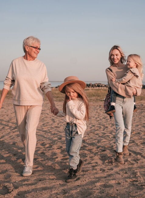 Großeltern und zwei Kinder spazieren Hand in Hand am Strand bei Sonnenuntergang