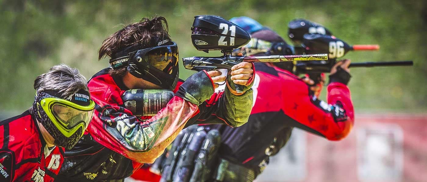 Gruppe von Paintball-Spielern in roten Trikots mit nummerierten Helmen während eines Wettkampfs auf freiem Feld.