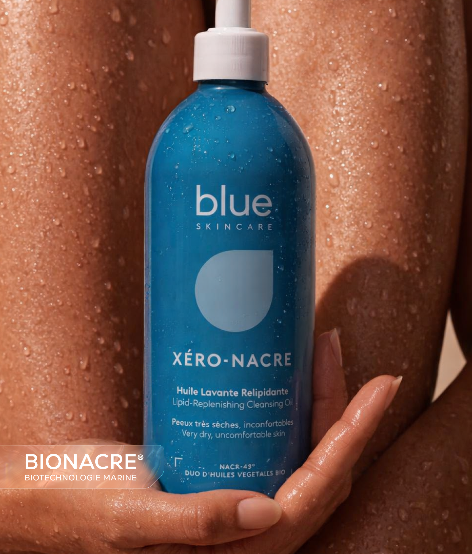 Flacon bleu de nettoyant huile lavante relipidante tenu à la main sur fond de peau mouillée avec gouttelettes d'eau