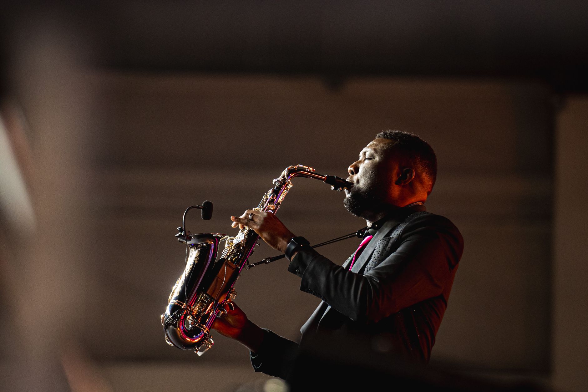 Saxophonist playing solo under stage lighting with dramatic red and warm spotlights