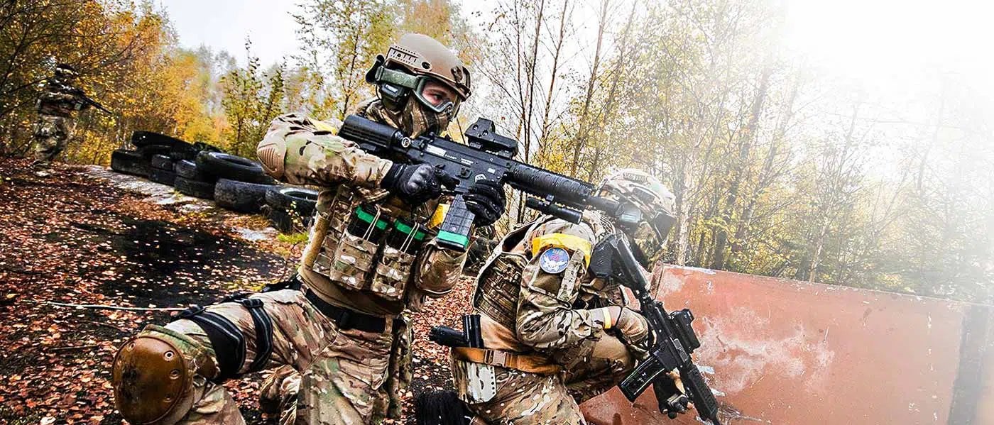 Zwei Paintball-Spieler in Camouflage-Ausrüstung mit Helmen und Schutzmasken halten Paintball-Markierer im Herbstwald.
